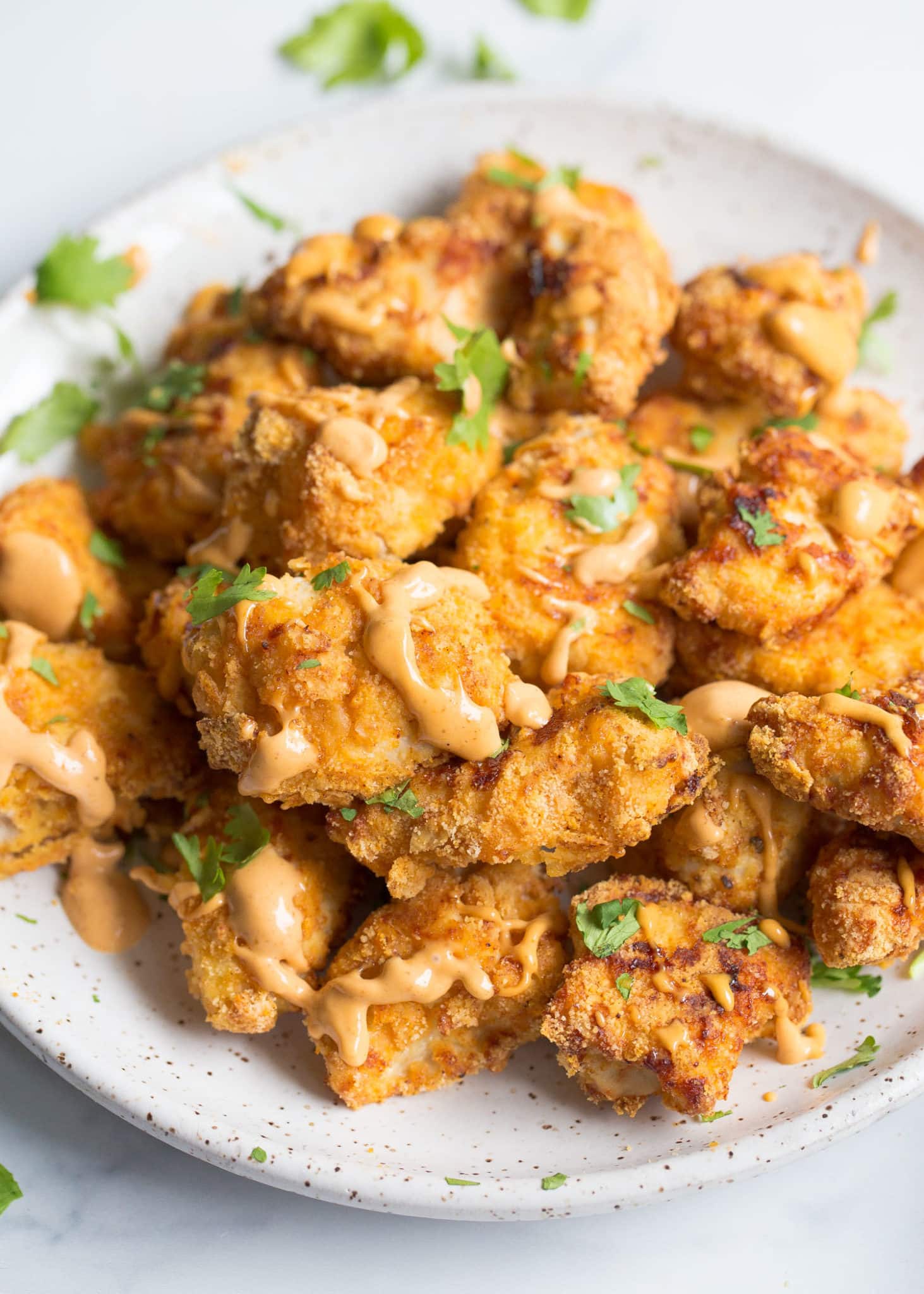 Chicken nuggets on a plate with sauce drizzle and chopped parsley