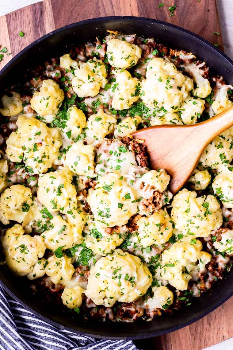 Creamy cauliflower and ground beef in a cast iron skillet with wooden spoon