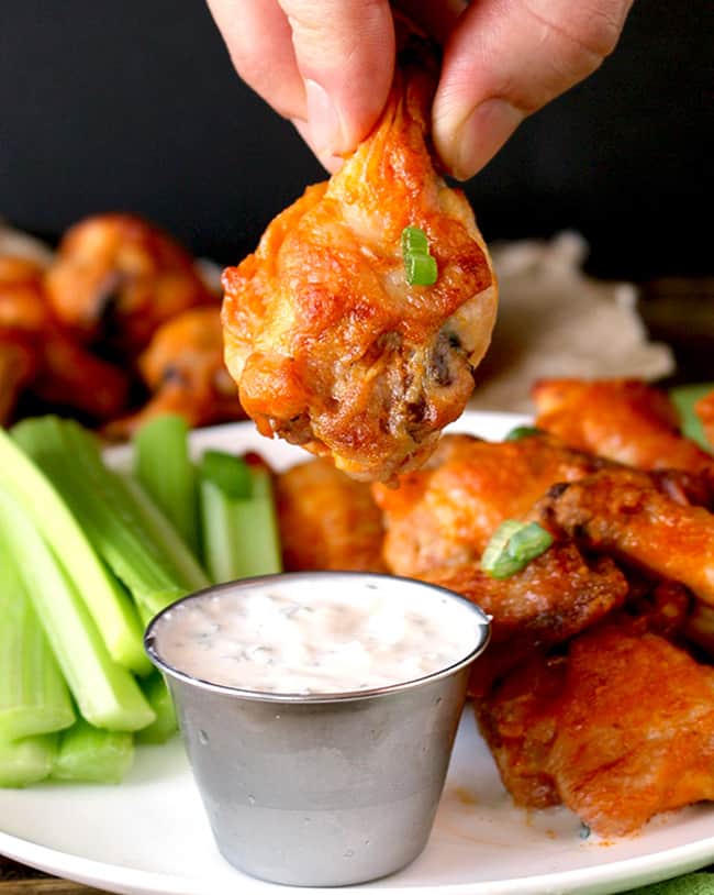 Baked buffalo wings with hand about to dip wing in ranch