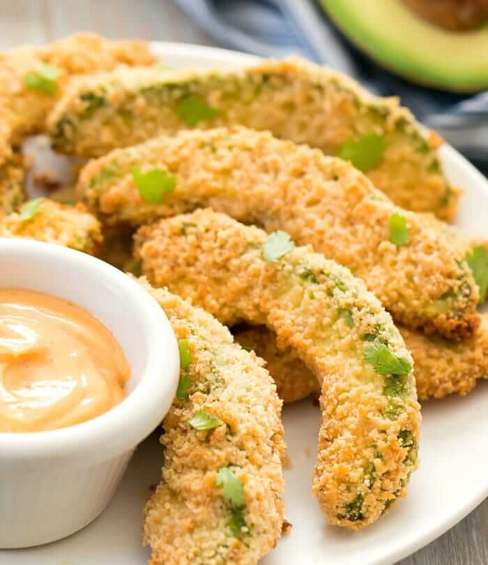 Breaded avocado wedges on a plate with dipping sauce