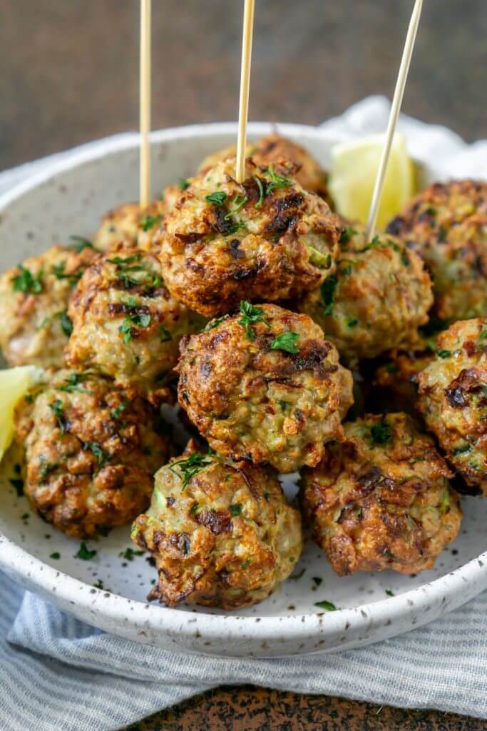 Pile of meatballs on a plate with lemon wedges and skewers in a few meatballs