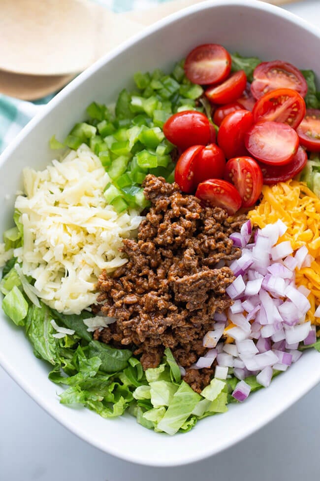 Salad plate with separate toppings of cheese, ground beef, red onion, tomato, bell pepper.