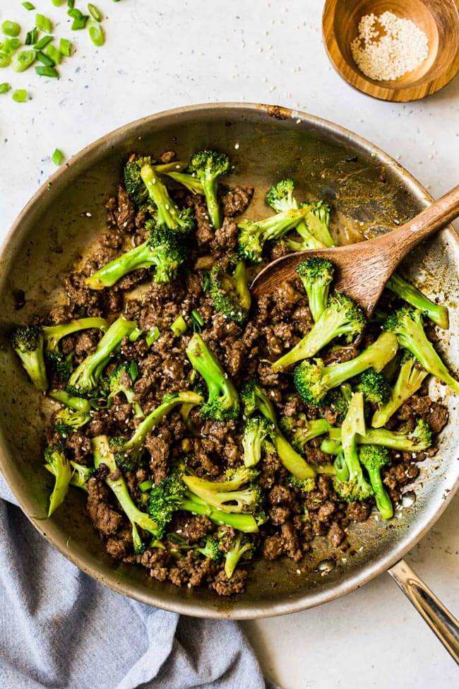 Ground beef and broccoli stir-fry in a skillet with wooden spoon