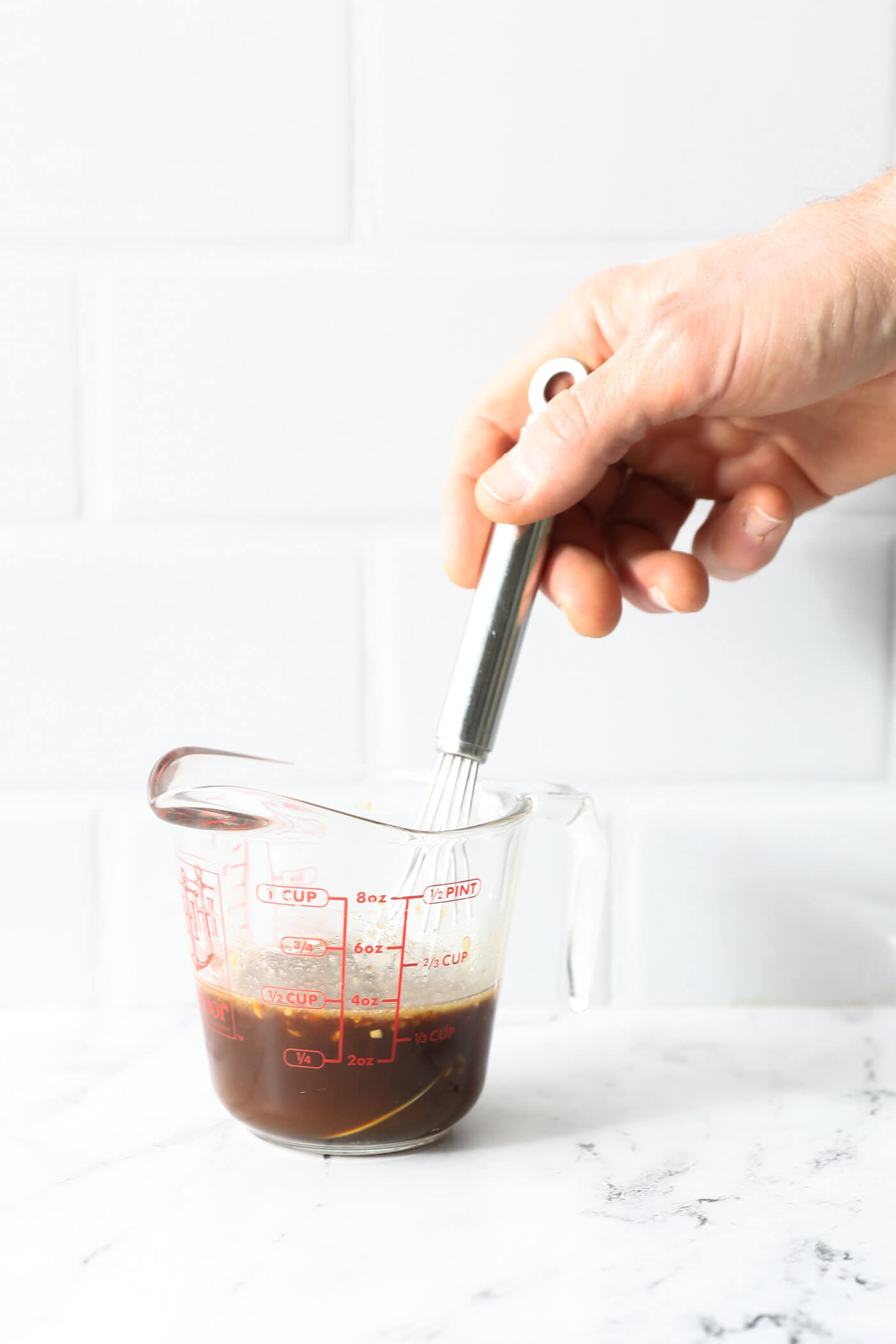 Stirring sauce in a glass measuring jar with a whisk.