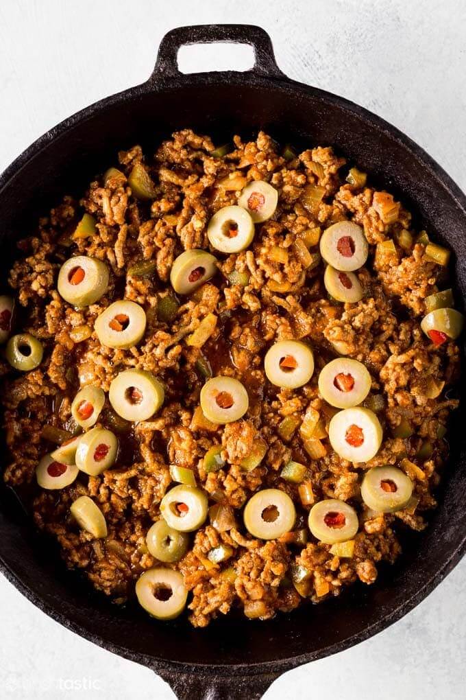 Low carb ground beef picadillo in a cast iron skillet topped with sliced green olives