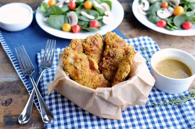 Baked chicken tenders in a basket with forks and salad behind