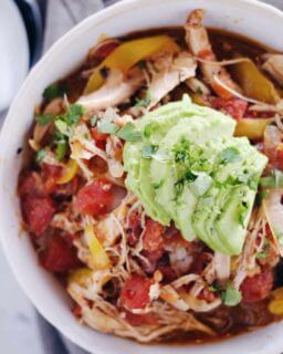 Crockpot chicken enchilada soup in a bowl with sliced avocado and onions on top
