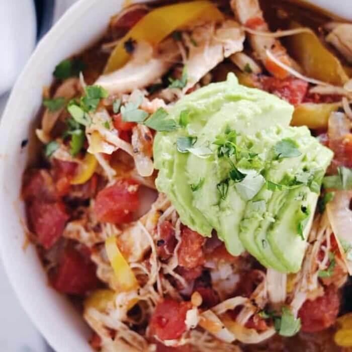 Crockpot chicken enchilada soup in a bowl with sliced avocado and onions on top