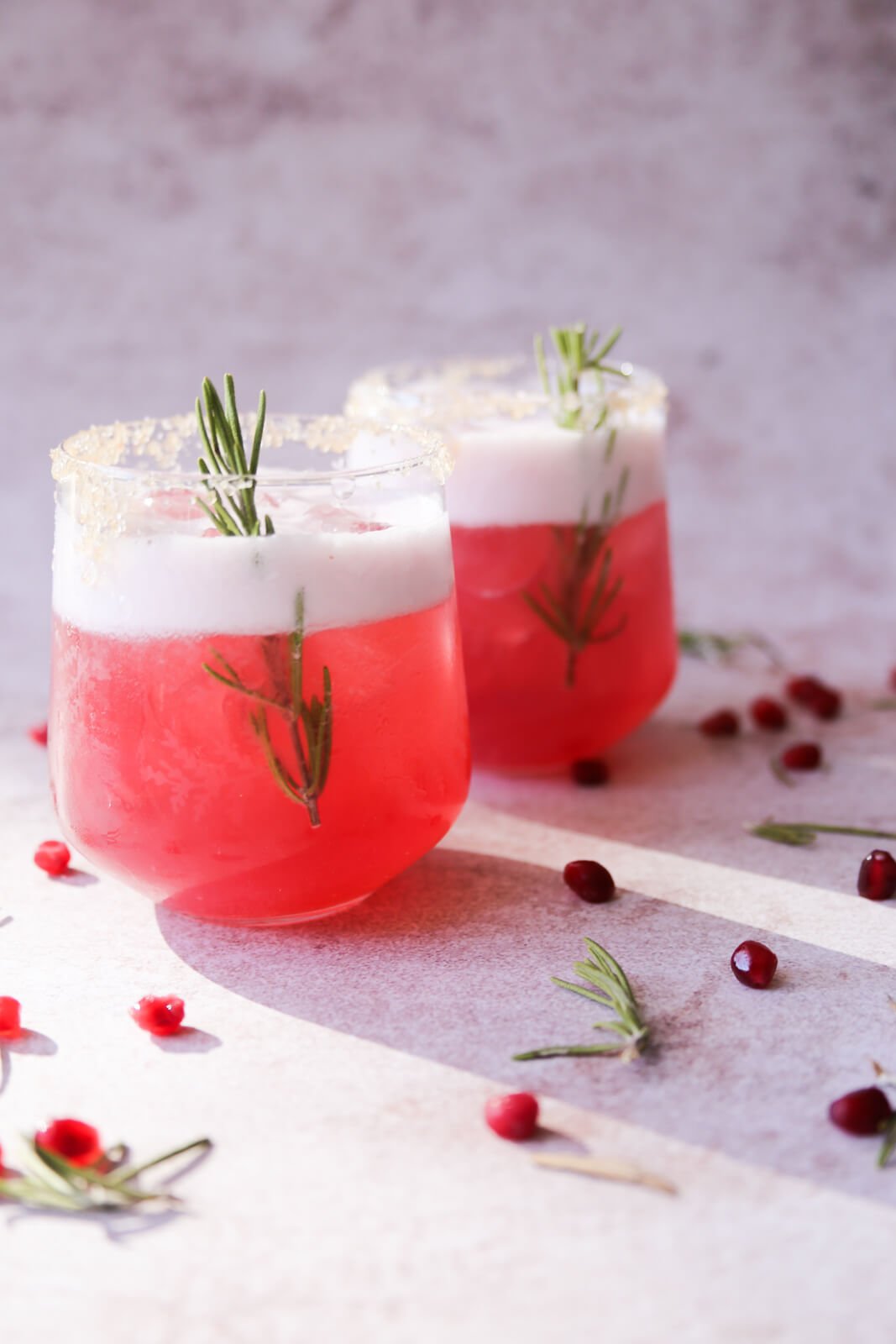 2 pink christmas margaritas in a glass with rosemary sprig