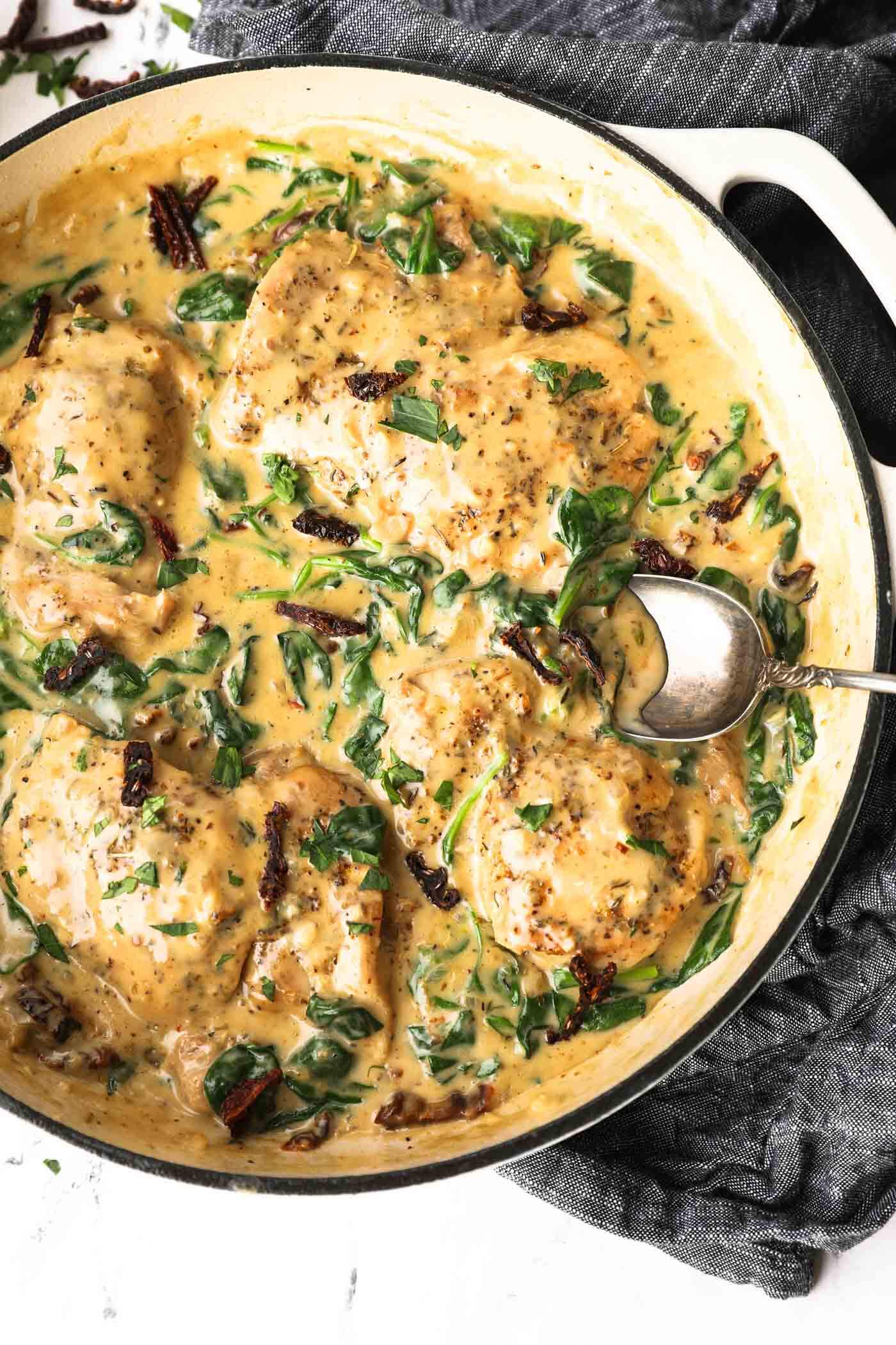 Overhead shot of dairy free creamy tuscan chicken with spinach and sun dried tomatoes and spoon coming out