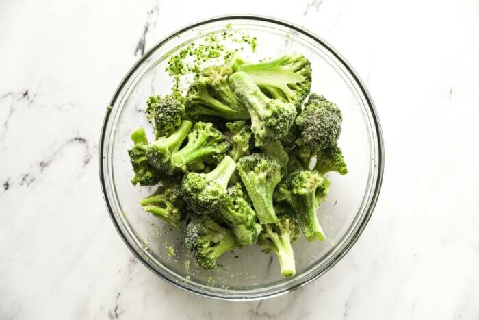 Frozen broccoli florets in a bowl tossed with seasoning