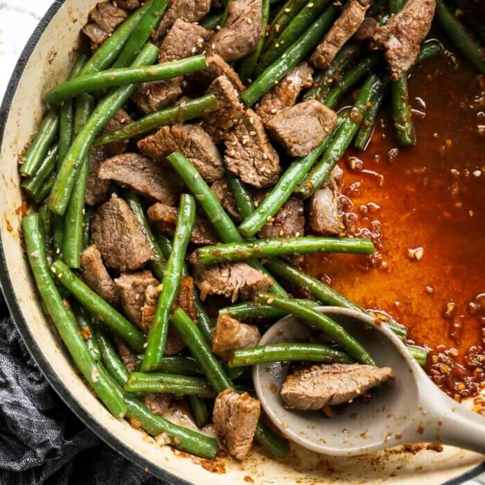 Overhead image of beef with garlic sauce in a pan with green beans and sesame seed toppings