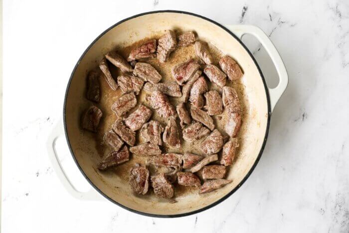 Cooked beef strips in a white cast iron pan