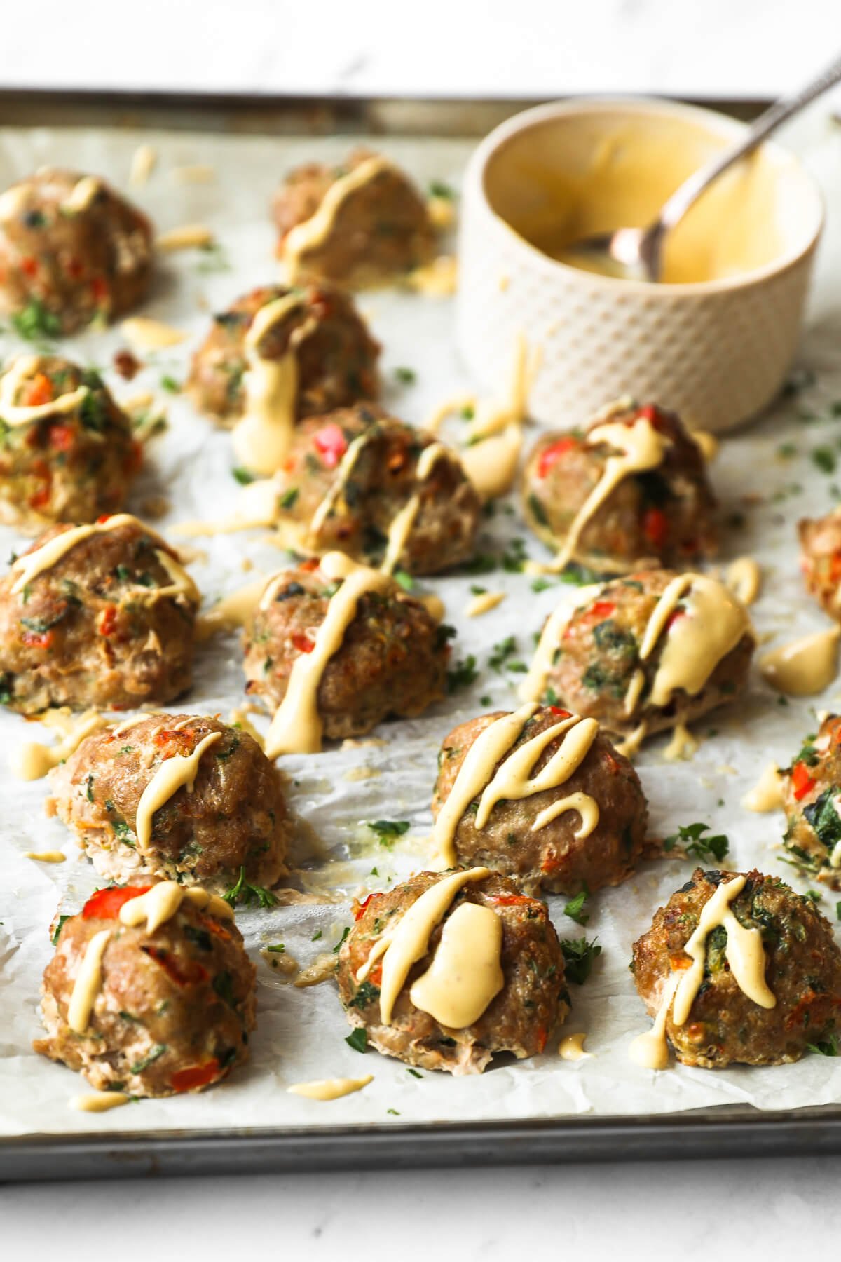 Angled image of keto meatballs on a sheet pan with spicy sauce drizzled on top. Front few meatballs are in focus with the rest and side of sauce blurred out in the background.