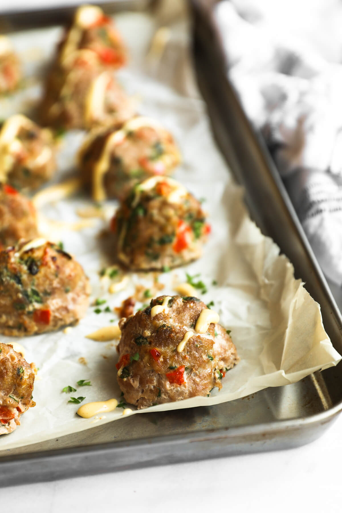 Angled image of turkey meatballs on a sheet pan with spicy aioli sauce drizzled on top. One meatball in focus with the rest blurred in the background.