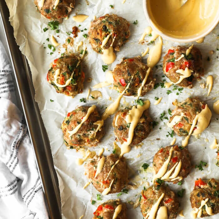 Overhead image of ground turkey meatballs on a sheet pan with spicy sauce drizzled on top. Extra sauce in a ramekin on the sheet pan.