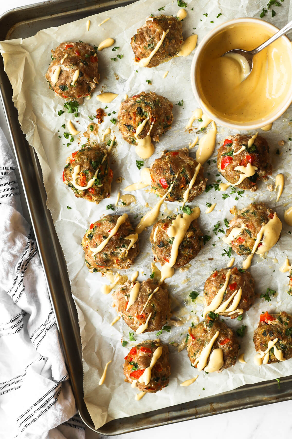 Overhead image of ground turkey meatballs on a sheet pan with spicy sauce drizzled on top. Extra sauce in a ramekin on the sheet pan. 