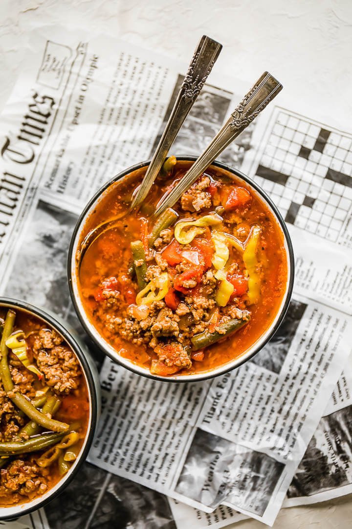 Two bowls of hamburger soup on a crumpled newspaper with spoons sticking out.