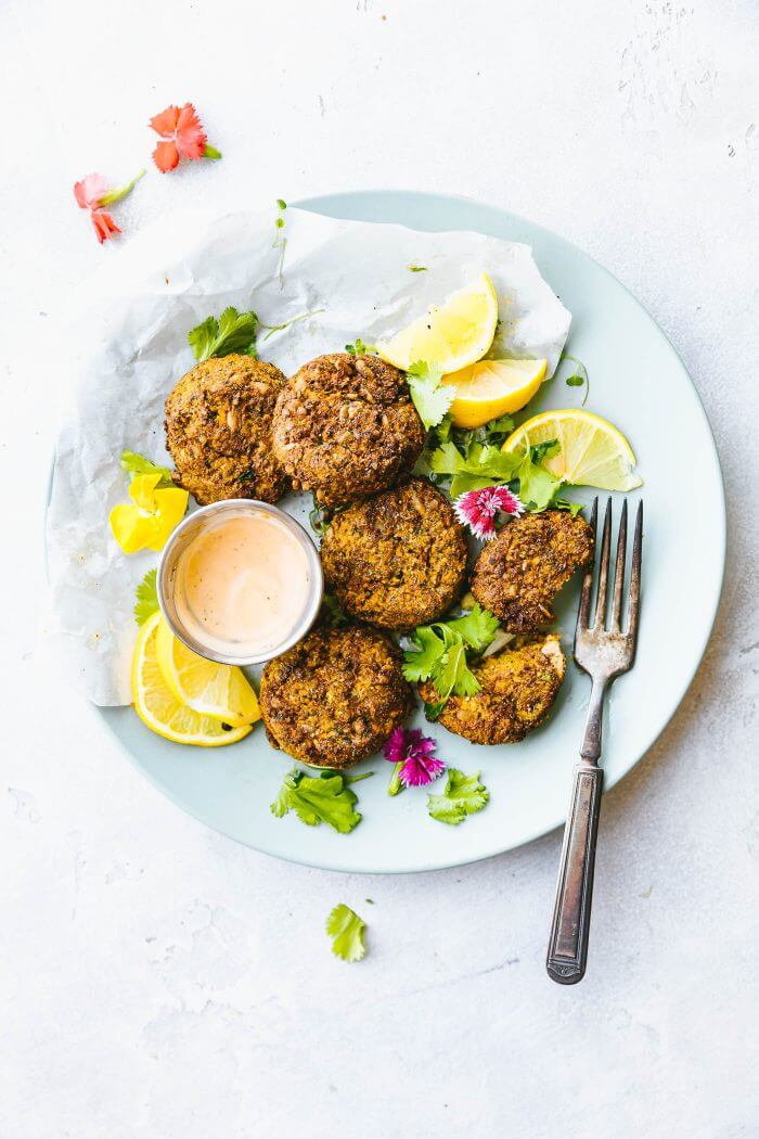 A plate of sweet potato cauliflower patties with fork and lemon wedges