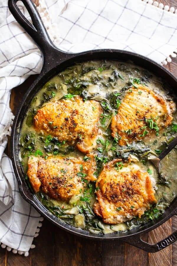Skillet with four chicken thighs and creamy spinach sauce