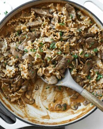 Creamy beef and mushrooms with noodles and scoops taken out of the skillet.
