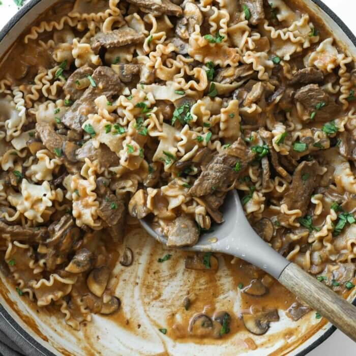 Creamy beef and mushrooms with noodles and scoops taken out of the skillet.
