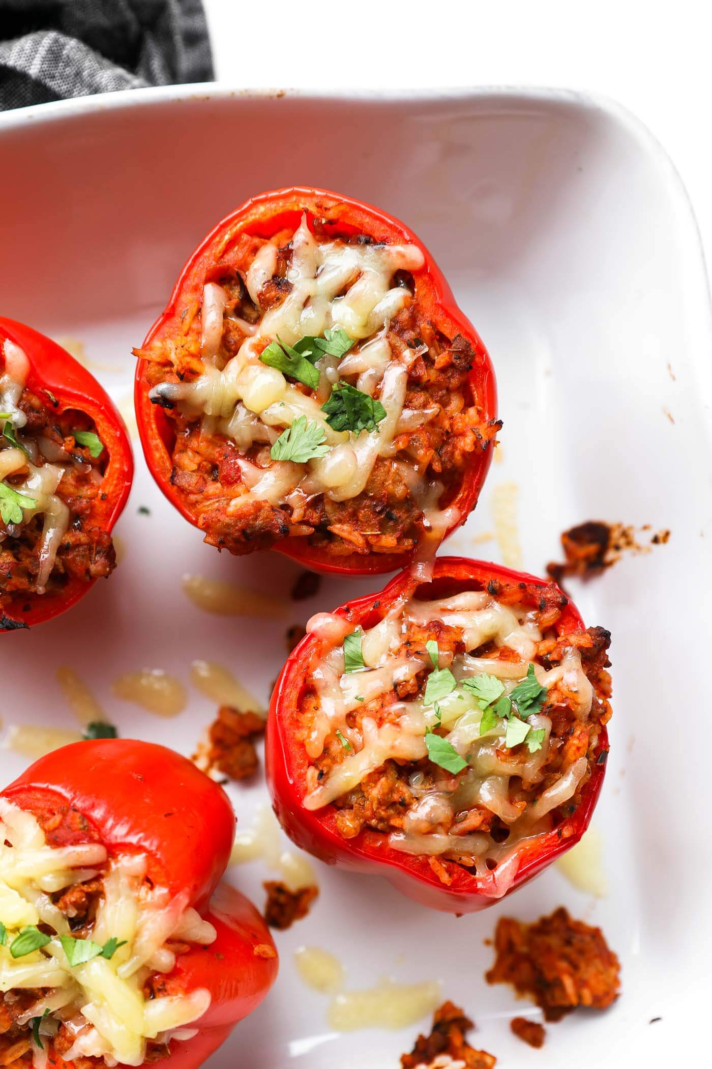 Overhead image of a baking dish with stuffed bell peppers in it. Melted cheese and chopped parsley garnish the tops.