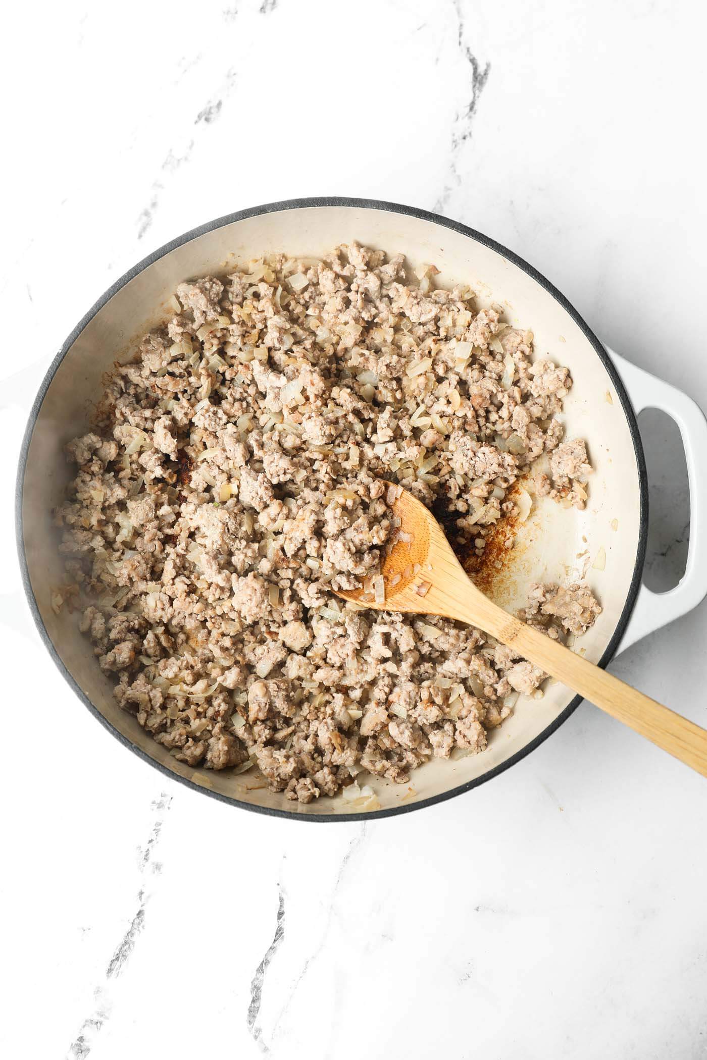 Overhead image of a skillet with ground pork browned in it. A wooden spoon is mixing it around.