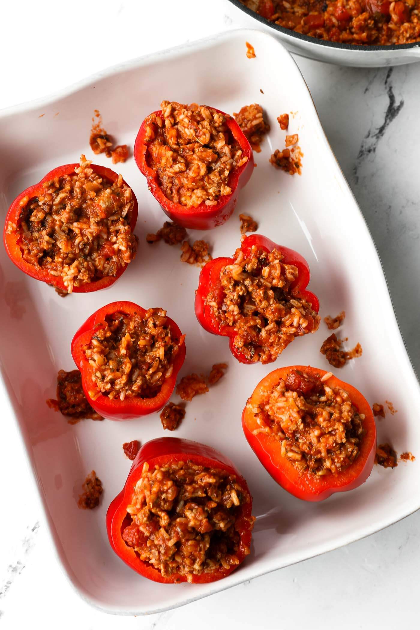 Six stuffed red bell peppers in a baking dish before they get cooked in the oven.