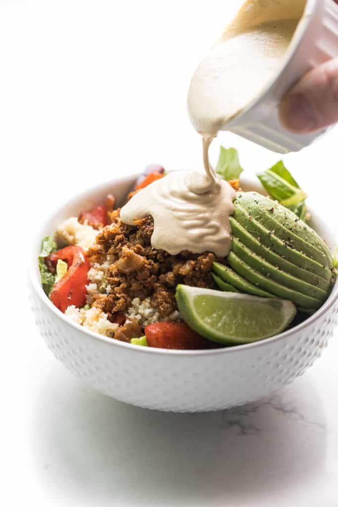 Ground beef burrito bowls with avocado, cauliflower rice and lime. Sauce pouring over the top.