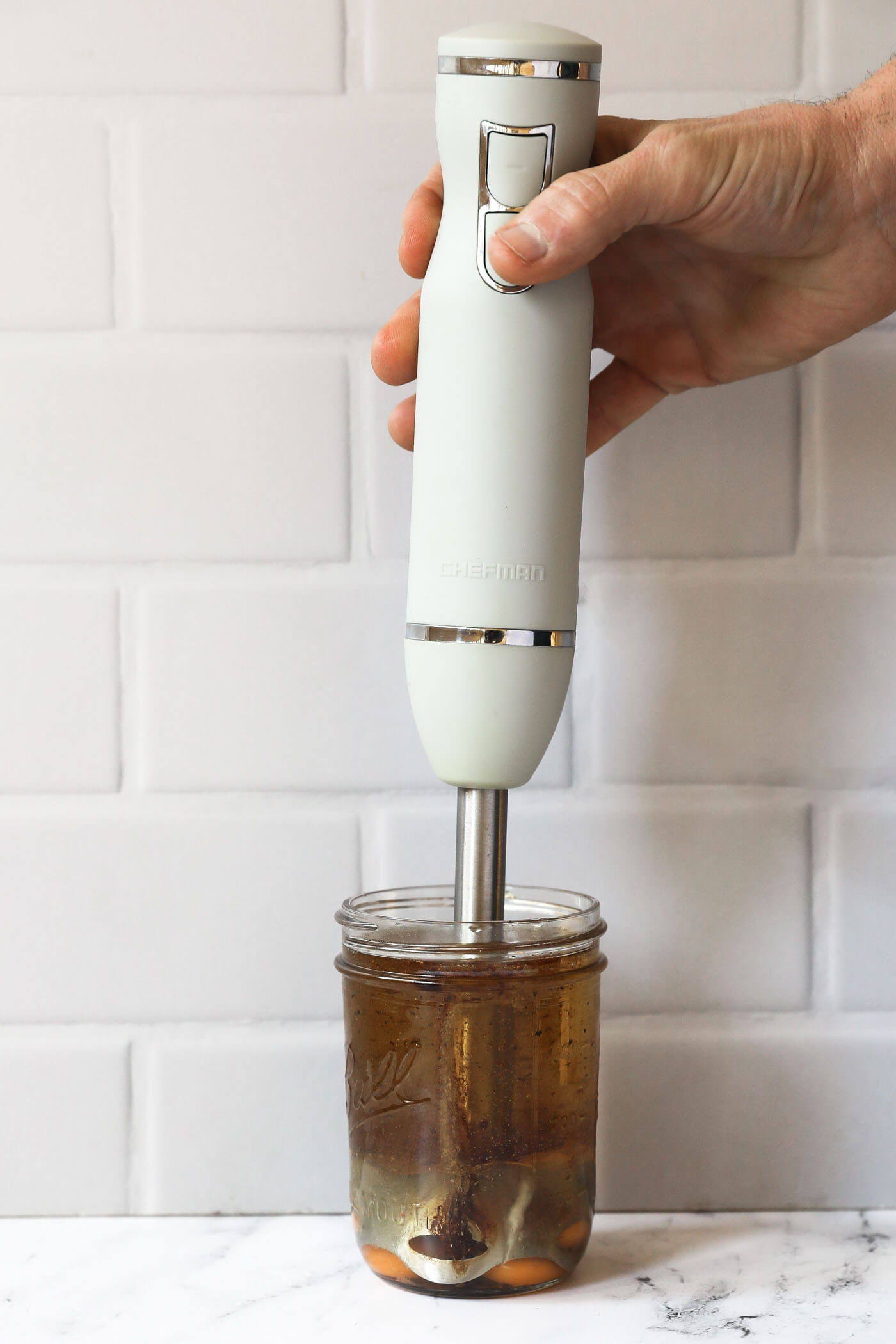 An immersion blender in a mason jar, about to be turned on to emulsify the ingredients.