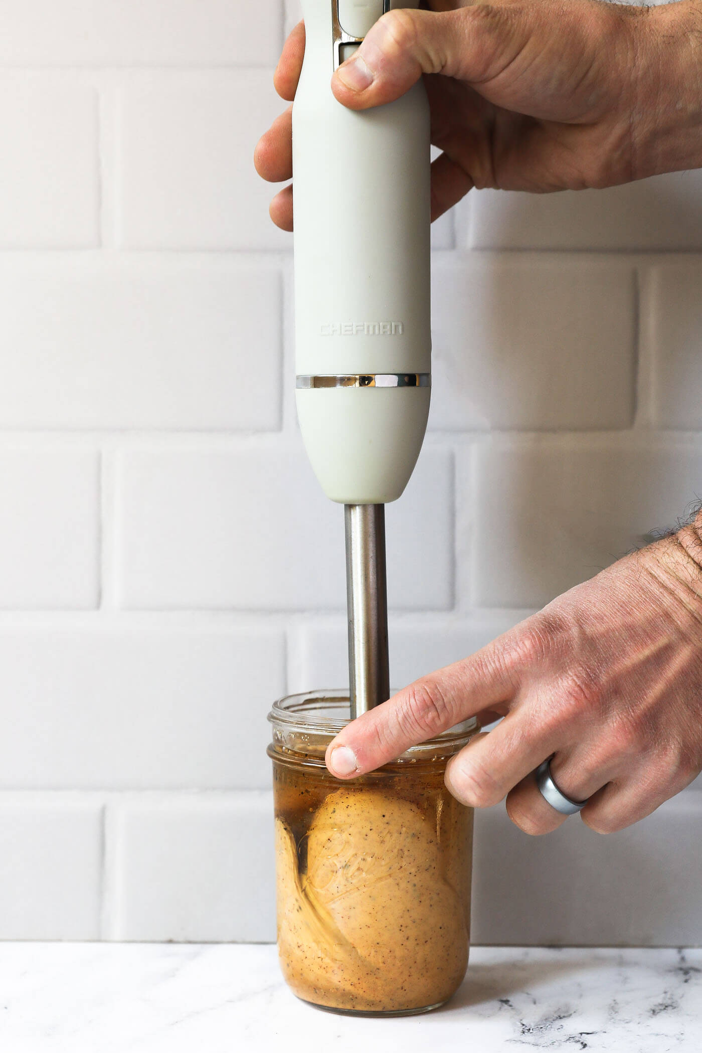 Someone using an immersion blender to emulsify a homemade chili aioli in a mason jar. The sauce is not quite fully emulsified yet.