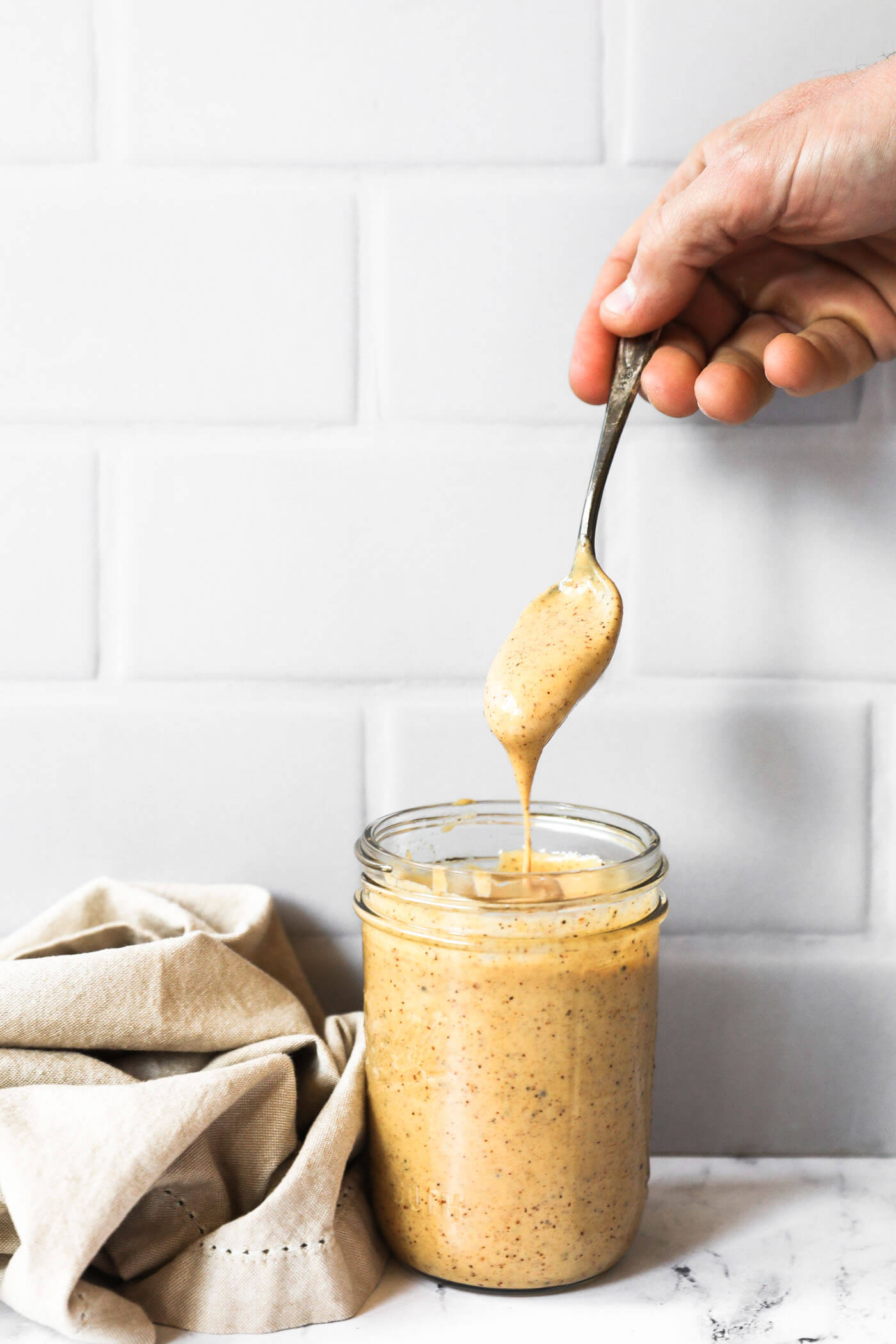 A hand pulling a spoon dipped in the chili aioli sauce out of a mason jar. The sauce is dripping off the spoon and back into the jar. 