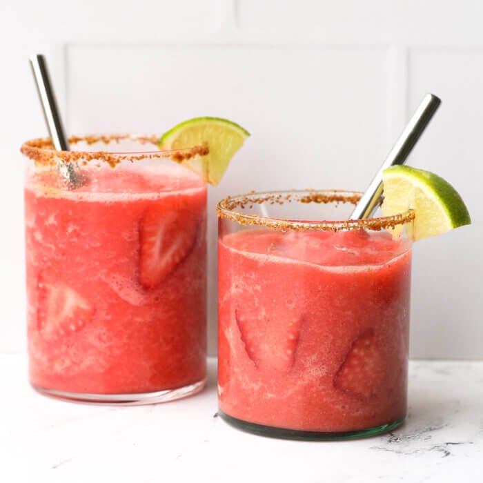 Two glasses of frozen strawberry daiquiri mocktails with brown sugar rim, lime wedge and straws