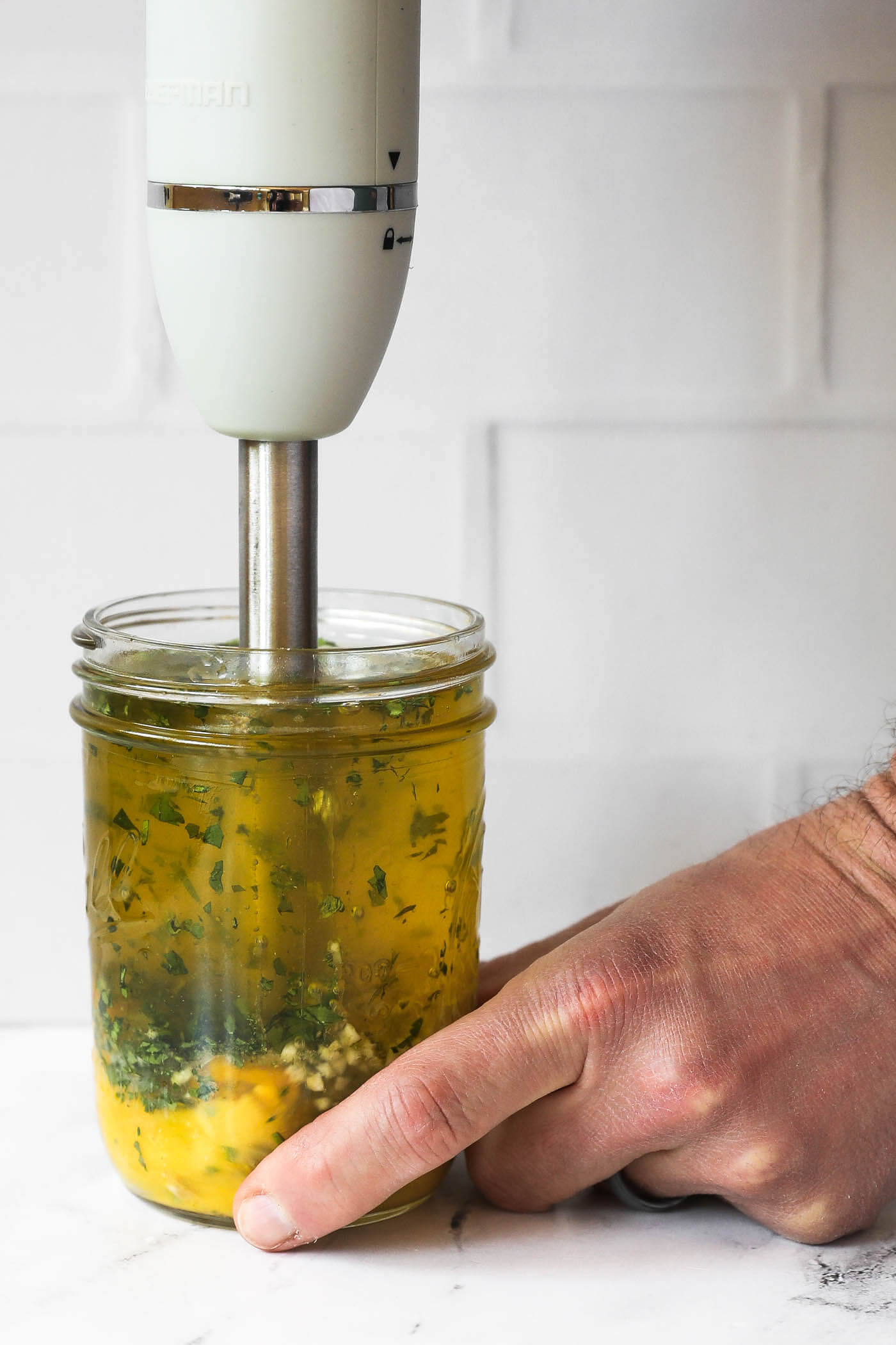 Someone putting an immersion blender in a mason jar full of cilantro lime aioli ingredients.