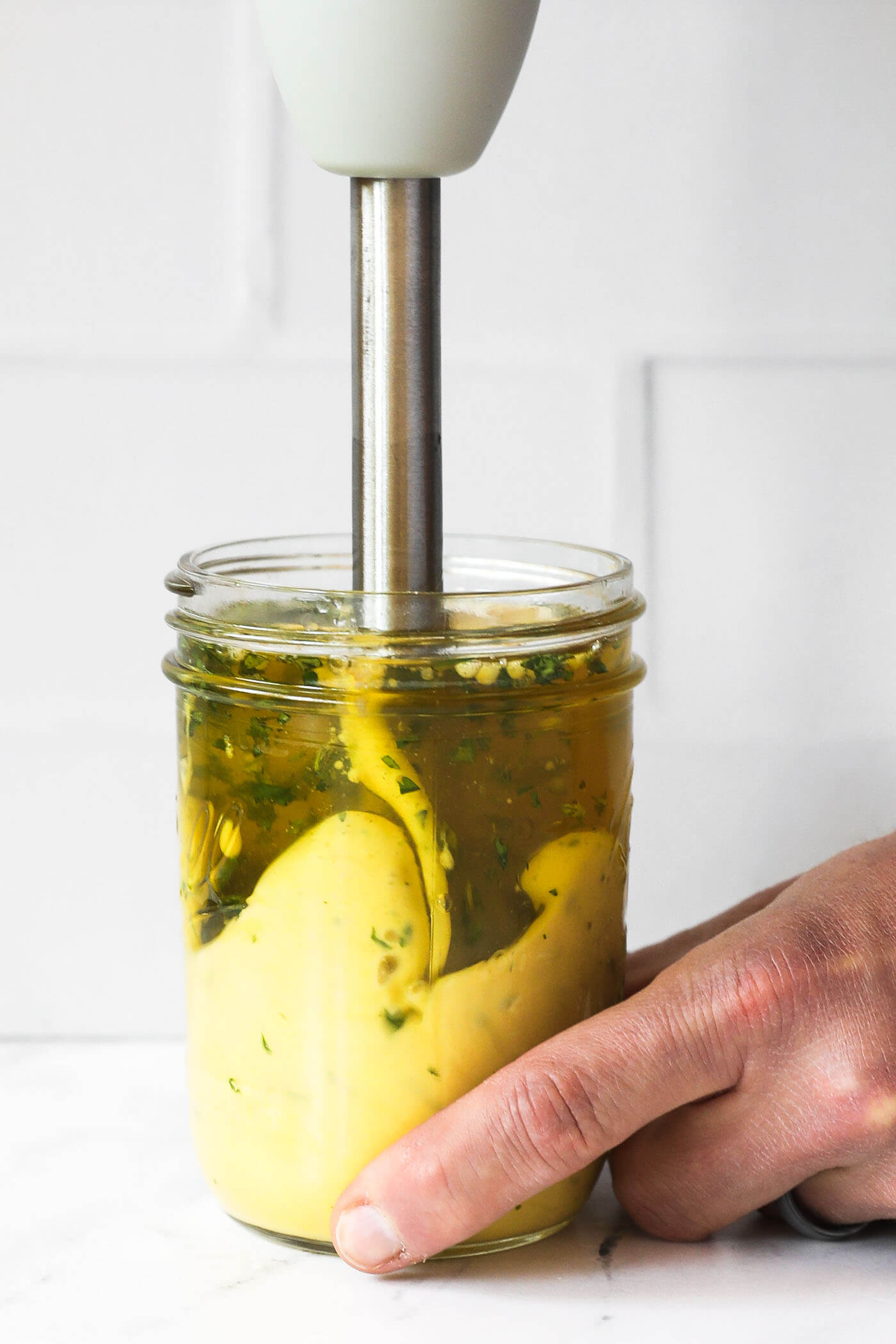 Someone emulsifying cilantro lime aioli in a mason jar with an immersion blender.