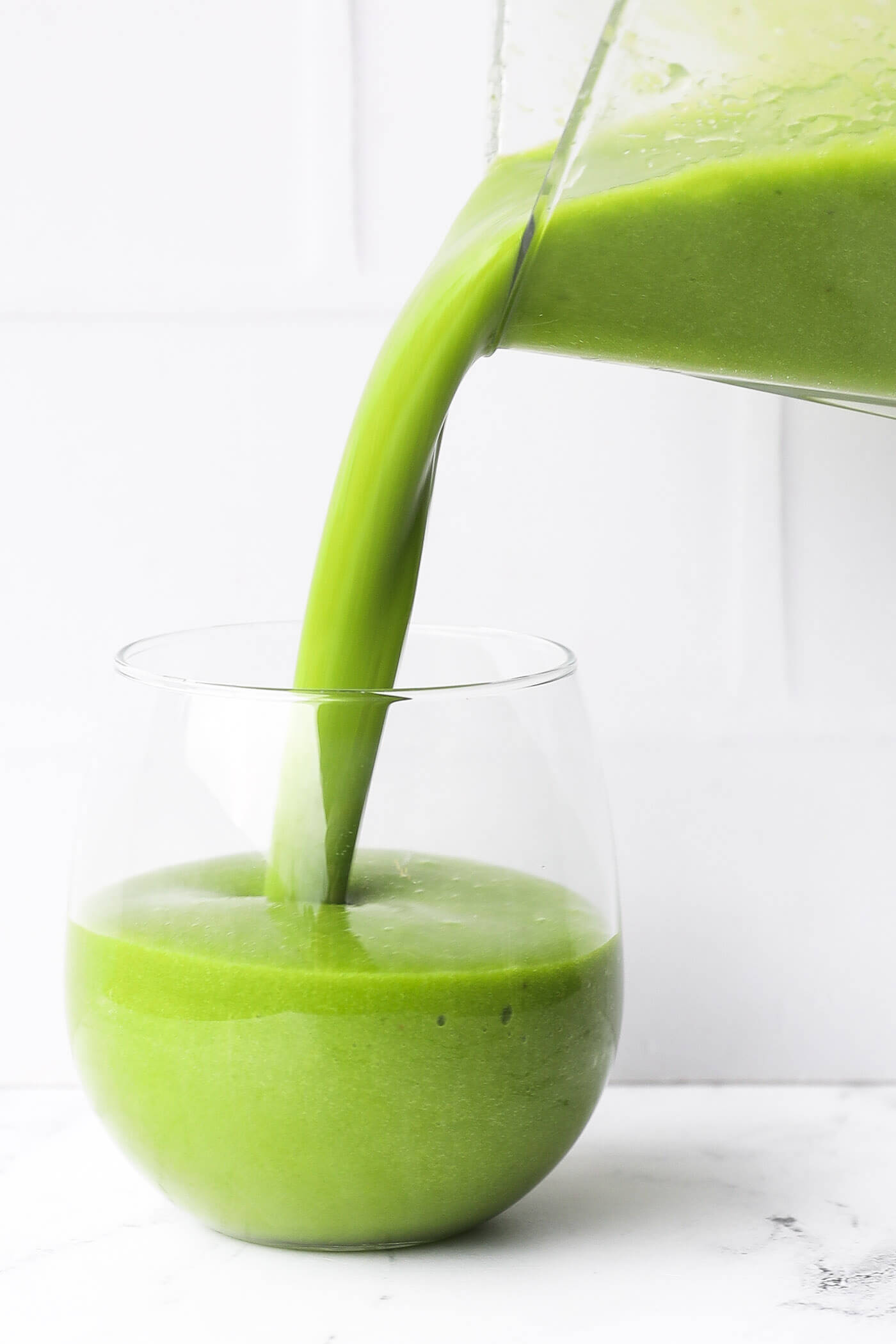 Pouring the vibrant green banana spinach smoothie into a glass.