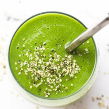 Overhead shot of the spinach smoothie in a glass with a straw and hemp seeds sprinkled on top.