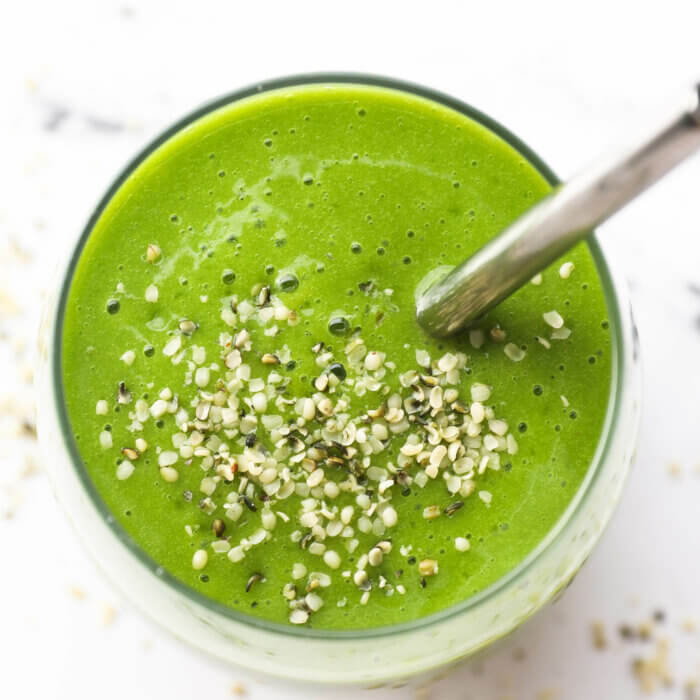 Overhead shot of the spinach smoothie in a glass with a straw and hemp seeds sprinkled on top.