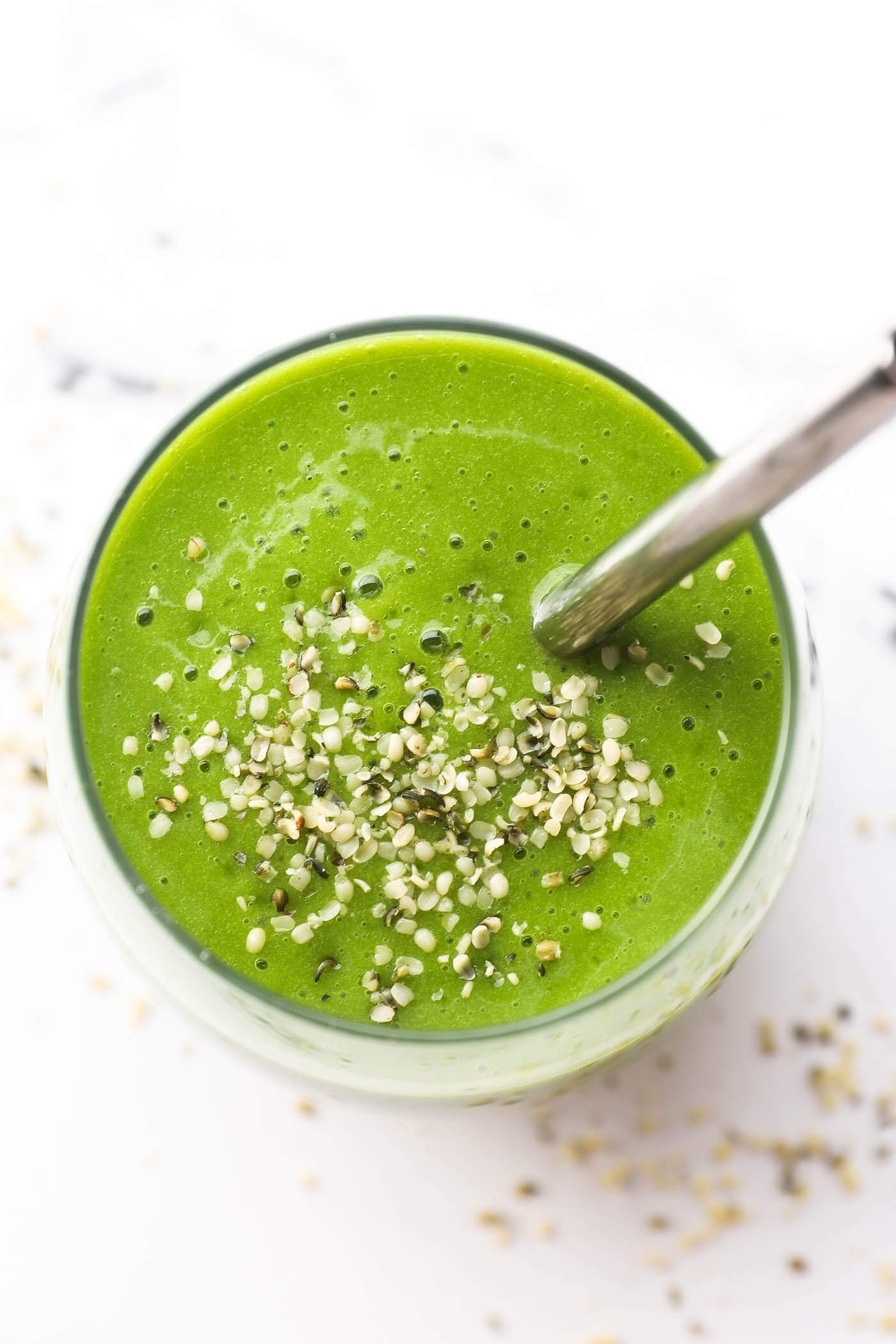 Overhead shot of the spinach smoothie in a glass with a straw and hemp seeds sprinkled on top.