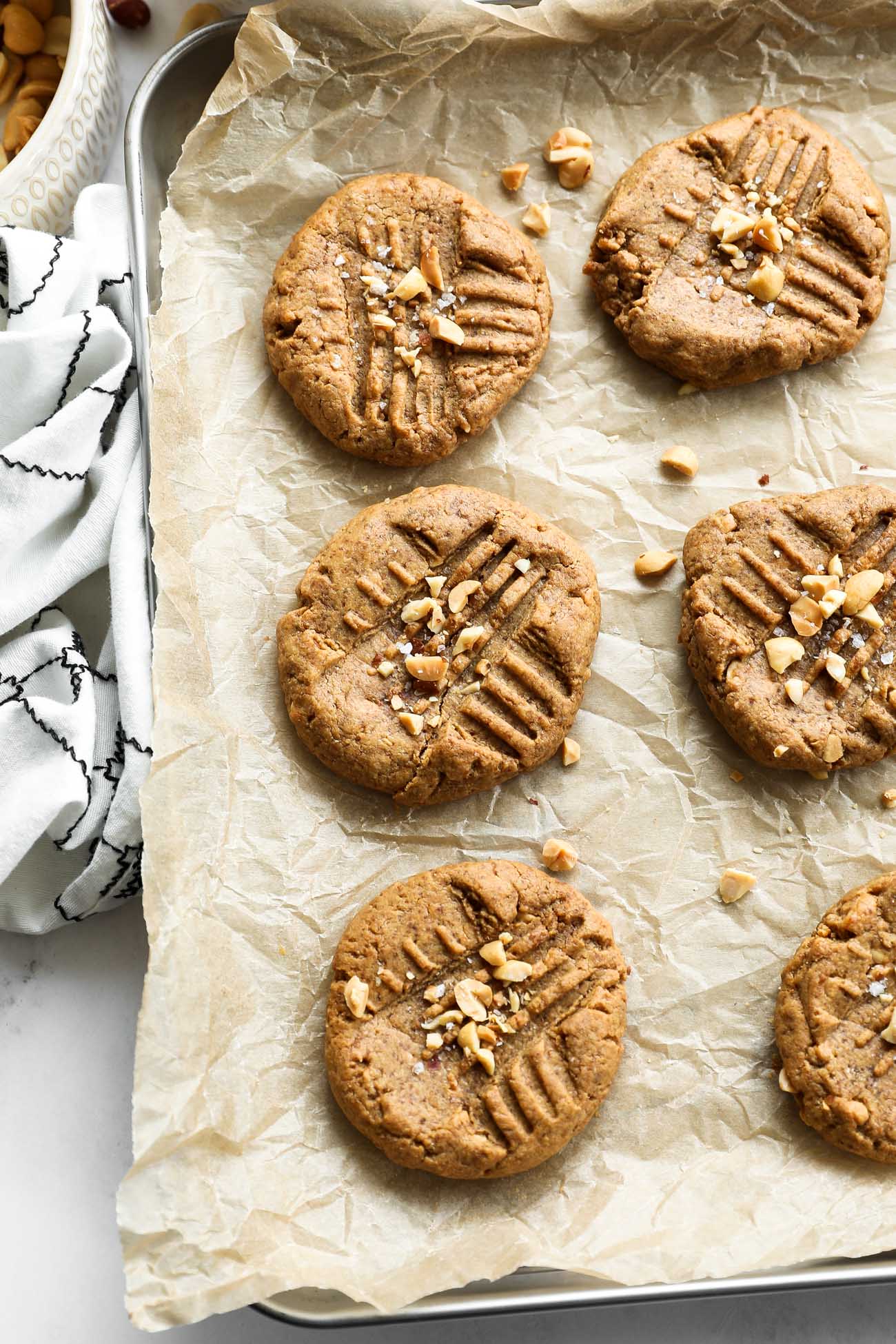 Overhead image of gluten free peanut butter cookies on a sheet pan. Cookies topped with chopped peanuts and flaky sea salt.