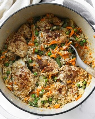 Overhead image of dutch oven chicken and rice with peas, onions and carrots.