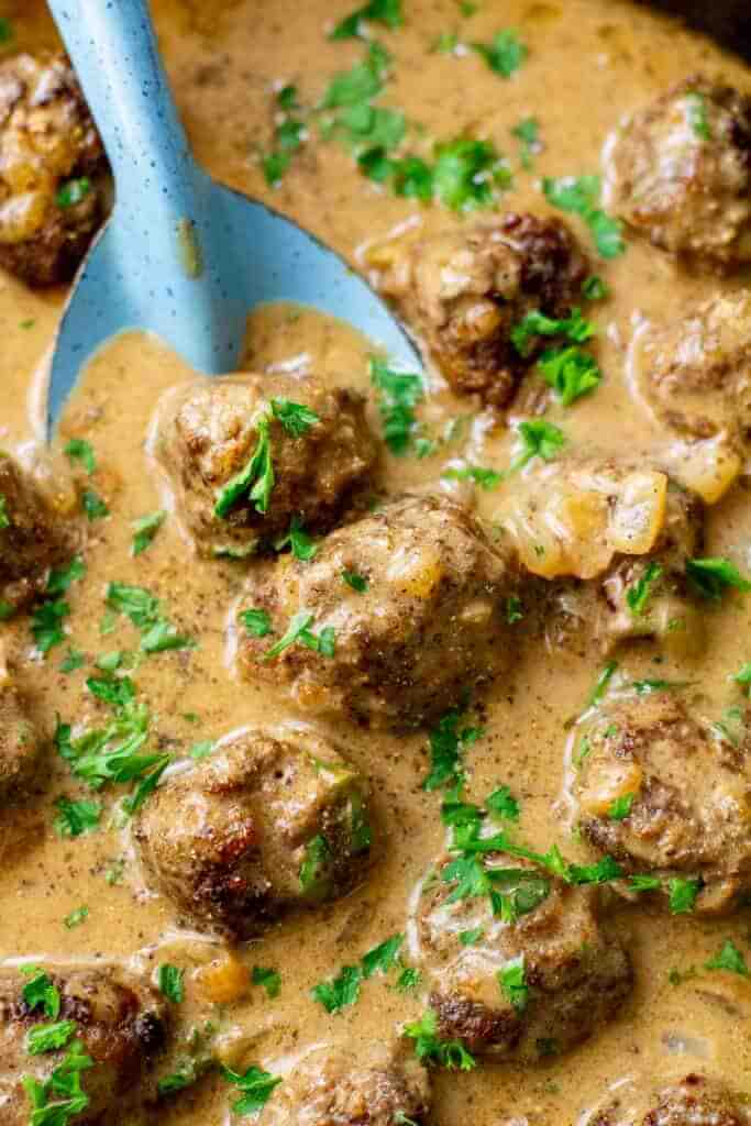 Swedish meatballs in a pan with sauce and spoon digging in.