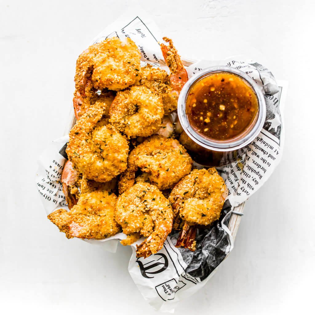 Air fryer shrimp in a newspaper lined basket with chili sauce on the side