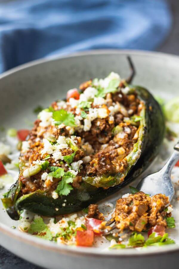 Stuffed poblano pepper on a plate with ground beef and cheese and cilantro topping.