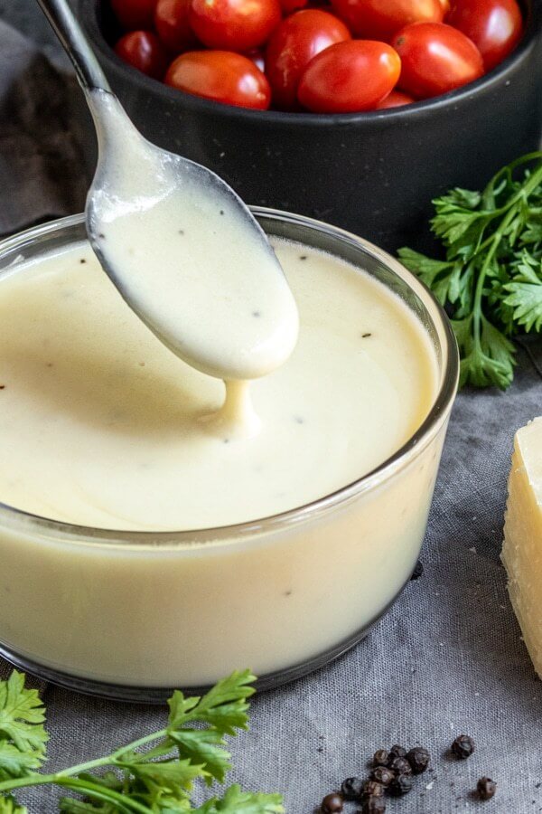 Angle image of keto alfredo sauce in a glass bowl with spoon coming out