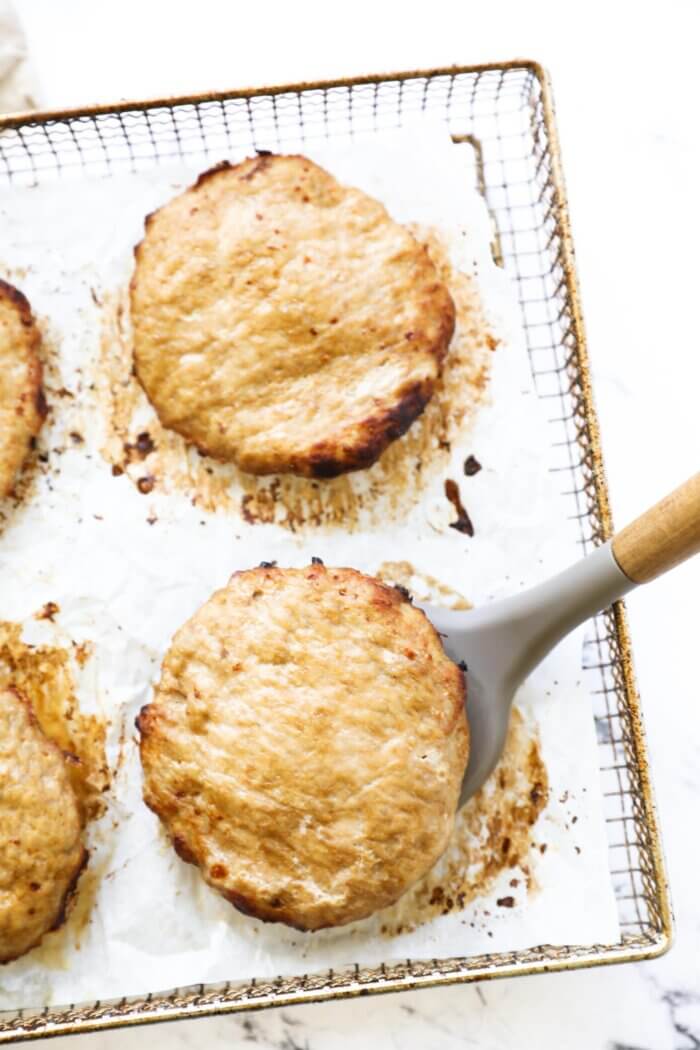 Turkey burgers in an air fryer basket with one patty being lifted by a spatula.