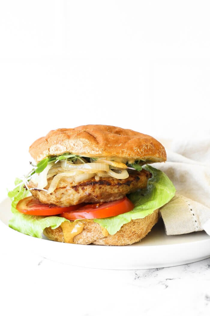 Image of a loaded turkey burger on a gluten free bun. Toppings include chipotle aioli, lettuce, tomato, turkey patty, caramelized onions and microgreens. 