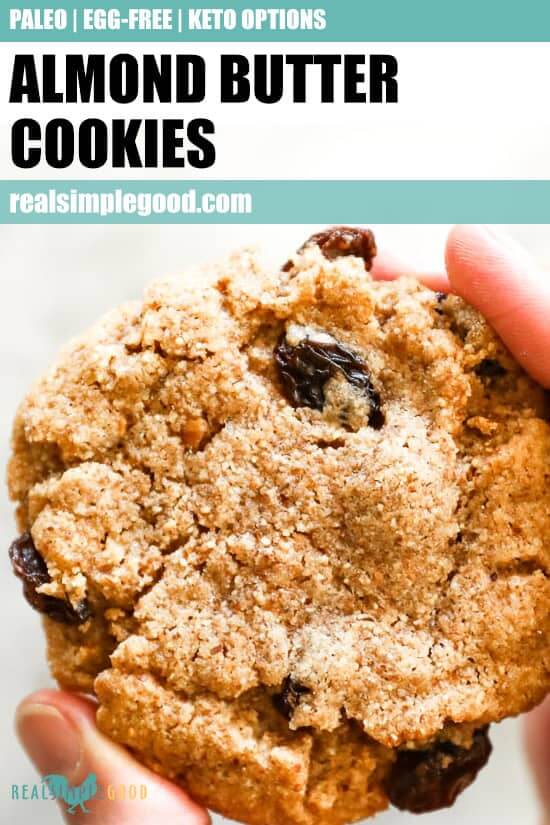 Close up on holding one almond butter cookie with text overlay at top for pinterest. 