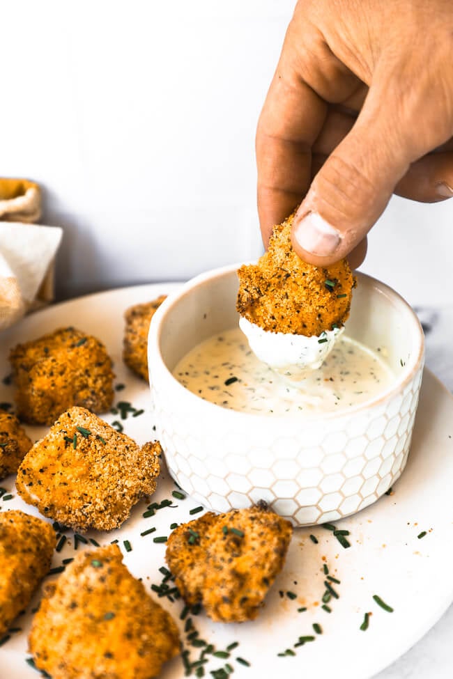 Angled image of dipping one air fryer chicken nugget into small bowl of ranch sauce. 
